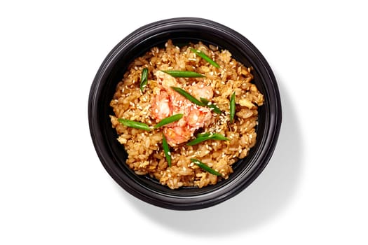 Wok rice with shrimps, eggs, green onions and sesame seeds in a black bowl on a white background