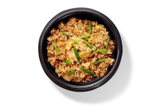 Overhead view of a tasty portion of chicken fried rice seasoned with sesame seeds and green onions, served in a black bowl