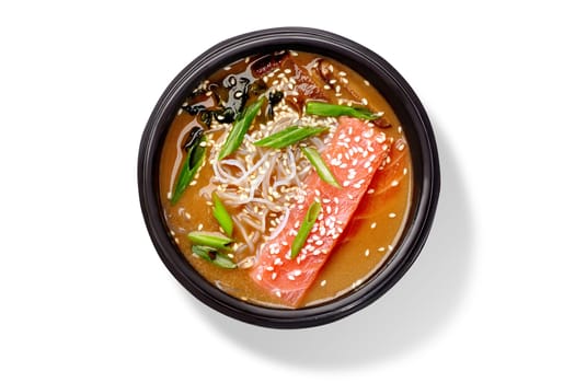 Miso soup with salmon, glass noodles, wakame seaweed, mushrooms, spring onions and sesame seeds served in black bowl, top view