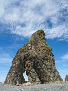 A rock tower under a bright blue sky with a few clouds at Ruby Beach in Washington.