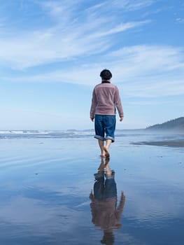 A woman walks barefooted on the beach on a sunny day along the coast of Washington State.