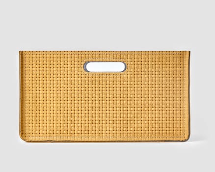 Close-up of a fashionable yellow leather handbag showcasing a woven texture and a unique cutout handle, set against a clean white backdrop
