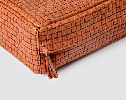 Close-up of the corner of a stylish brown woven leather bag, highlighting the intricate woven pattern and zipper detail