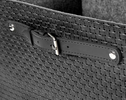 Close-up of a stylish black leather basket highlighting the woven texture and a fastened strap with a silver buckle