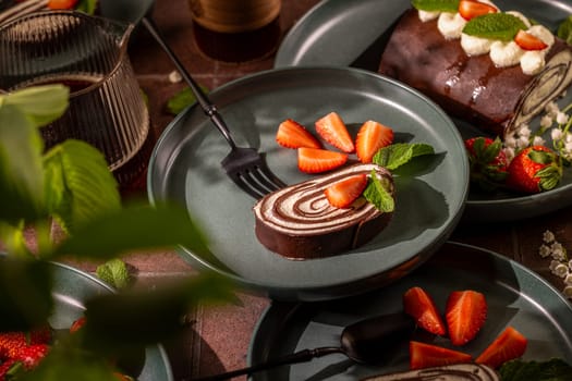 Delicious chocolate swiss roll elegantly served with fresh strawberries and mint leaves on a dark plate, creating a tempting dessert scene