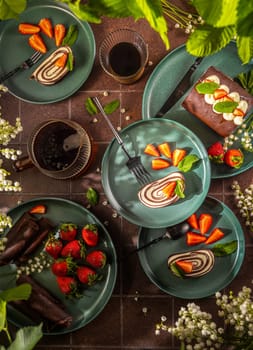 Pinwheel cake slices served on green plates with fresh strawberries and mint leaves, accompanied by cups of coffee, creating a delightful dessert setting