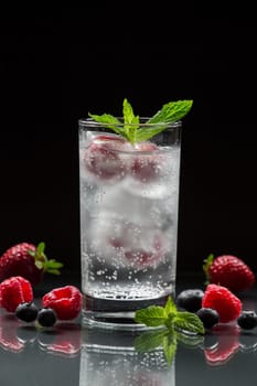 Iced water captures freshness with floating berries and mint, serving as the perfect drink for relaxation. The bright colors contrast beautifully against the dark backdrop.