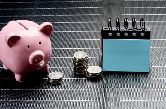 Pink piggy bank next to stacks of coins and desk calendar, symbolizing savings and financial planning, on dark background.