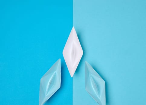 A white origami paper boat symbolizing leadership leads two blue boats on a two-tone blue background.