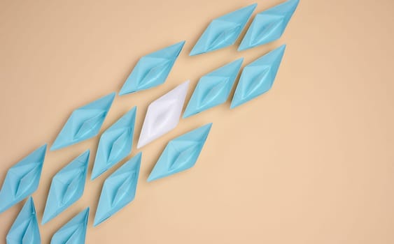 A white origami paper boat stands apart from a group of blue ones, symbolizing uniqueness or leadership, against a neutral background.