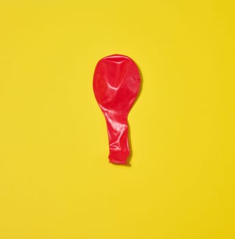 One red deflated balloon lies on a yellow background.