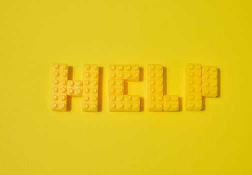 The word HELP, made from yellow toy blocks, is placed on a yellow background