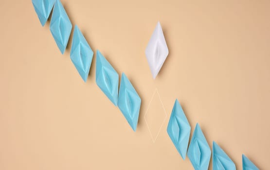 A line of blue origami paper boats with one white and the outline of the missing one, symbolizing uniqueness or a missing element, are placed on a neutral background