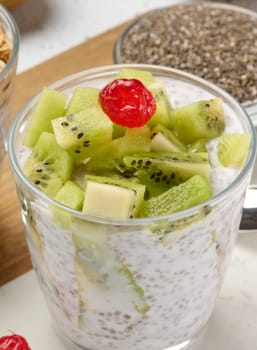 Yogurt and chia seed pudding in a glass, kiwi pieces. White table