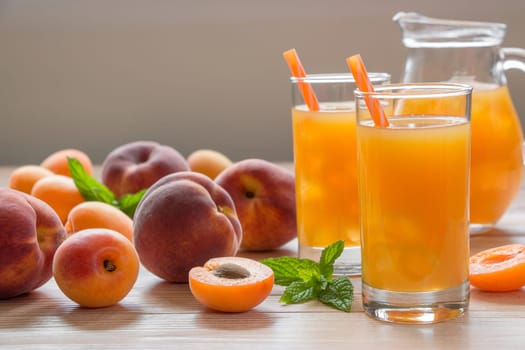 Delicious juice blends made from ripe apricots and peaches are served in clear glasses. Fresh fruits are arranged on a wooden table, adding a natural touch to the setting.