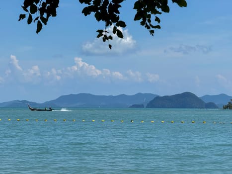 Wooden boats in a clear turquoise lagoon near Thailand tropical paradise scene showing motorboats in a stunning blue bay. Exotic coastal cliffs with greenery and palm trees on the coastline.