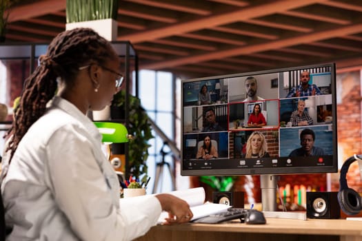 Team leader speaking with employees during videocall from home, looking over paperwork, organizing job shifts. African american supervisor doing teleconference with staff members, checking documents
