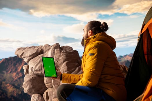 Mountaineer stands at the peak with satisfaction and uses mockup screen, hiker admires breathtaking view with crisp air on mountain top. Scenic surroundings highlights determination.