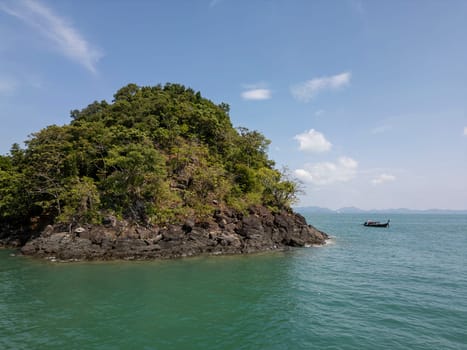 Aerial view of wooden boat cruising along a blue tropical lagoon, scenic seaside landscape of a sailboat on crystal clear water. Thai paradise of lush coastal cliffs and small islands.