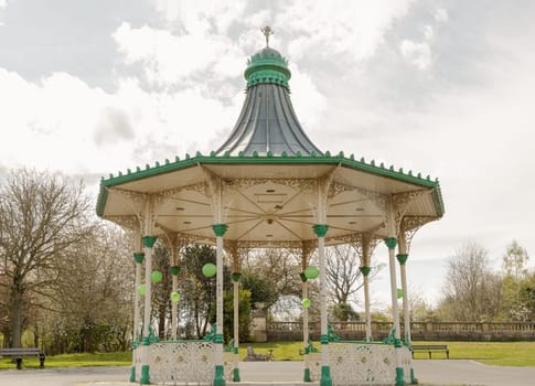 Newcastle, UK - Apr 13, 2025 - View of A Bandstand And A Grandstand. It’s a modern replica of the Victorian bandstand that had been installed in the Leazes park. The Music Pavilion with Green trees in the background, use it as your Wallpaper, Poster and Space for text, Selective focus.