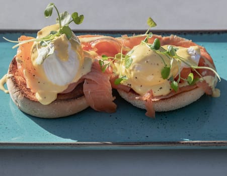 Eggs Royale made with english muffin, oak smoked salmon, a brace of poached hen's eggs & hollandaise sauce and watercress served on blue ceramic tray. use it as your Wallpaper, Poster and Copy space, Selective focus.