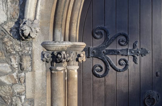 Royal Tunbridge Wells, UK - Apr 29, 2025 - Sunlight shines through on the surface of Ornamented wooden gate, Details exterior of Old gothic medieval church wooden door and sandstone arched with decorative wrought iron hinge. use it as your Wallpaper, Poster and Copy space, Selective focus.