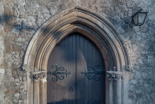 Royal Tunbridge Wells, UK - Apr 29, 2025 - Detail exterior of Old gothic medieval church wooden door and sandstone arched with decorative wrought iron hinge. Sunlight shines through on the surface of Ornamented wooden gate, use it as your Wallpaper, Poster and Space for text, Selective focus.