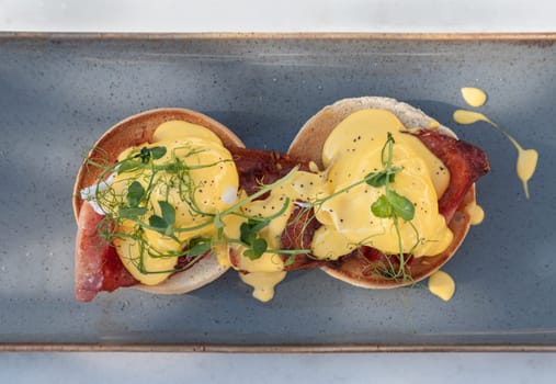 Top view of Eggs Benedict made with english muffin, grilled bacon, a brace of poached hen's eggs & hollandaise sauce and watercress served on ceramic tray. use it as your Wallpaper, Poster and Space for text, Selective focus.