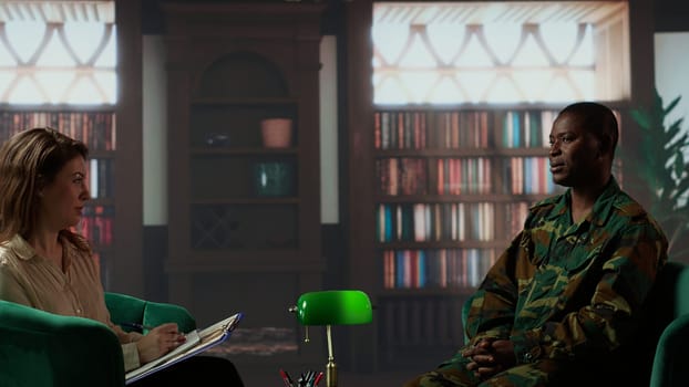 African american serviceman in camouflage uniform sits in therapy, looking depressed and opening up about combat scenes. War veteran soldier dealing with PTSD, reintegration program. Camera B.