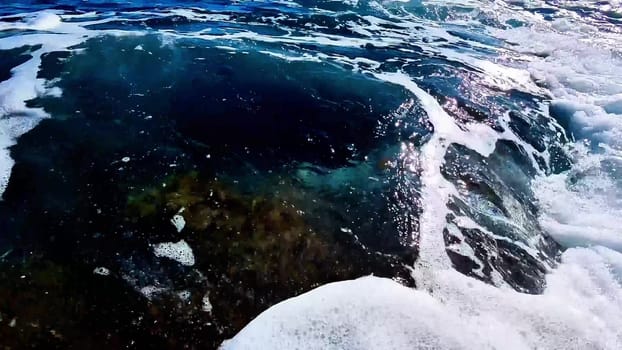 The stunning view shows ocean waves crashing against rocks, creating foamy patterns on the rugged terrain