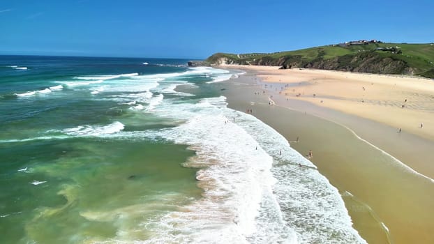 A stunning aerial view showcases a beautiful beach with golden sands and vibrant waves beneath a clear blue sky