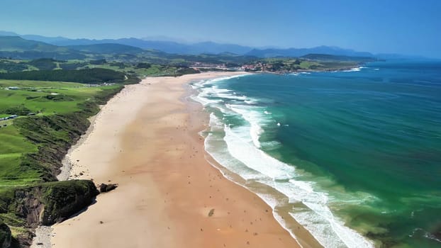 A stunning aerial view of a beautiful beach with clear turquoise waters, waves, and lush greenery nearby