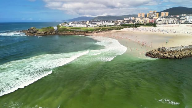 A stunning aerial shot captures a vibrant beach scene, showcasing beautiful waves and beachgoers enjoying the sunny day