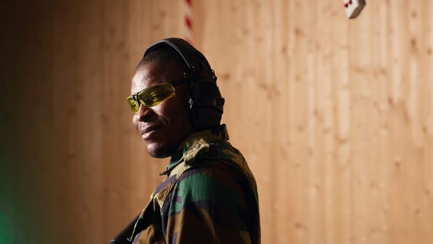 Portrait of happy military personnel using tactical operations equipment, shooting assault rifle. Smiling man in firing range preparing for mission, practicing with semiautomatic weapon, camera B