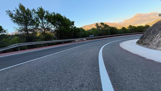 A winding road winds through majestic mountains, lush greenery, and clear blue skies, ideal for adventurers