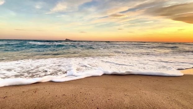 A tranquil scene of gentle waves softly caressing the golden shore during a stunning and colorful sunset