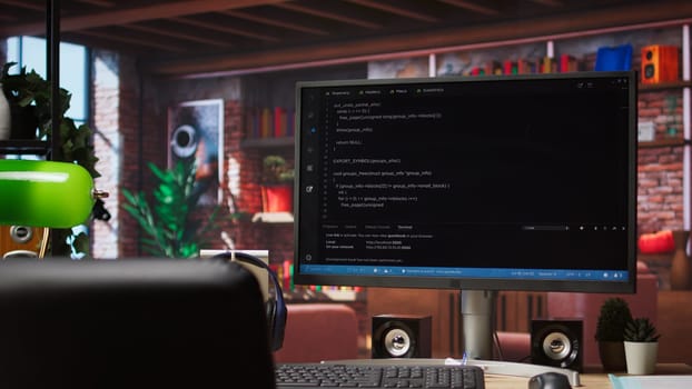 Computer desk with coding application on monitor used for creating software, implementing algorithms. Code editor on PC display used to build applications in cozy bright living room
