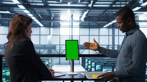 Programmers in data center brainstorming, using mockup tablet, observing equipment analytics. Server hub IT coworkers use isolated screen device, adjusting system parameters, camera B