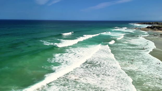 Enjoy a breathtaking aerial view of the tranquil ocean waves and the vibrant turquoise waters below a clear blue sky