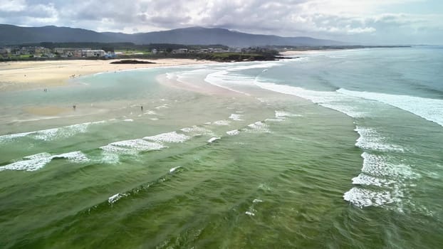Beautiful aerial view showcasing a tranquil beach with gentle waves and mountains in the background.