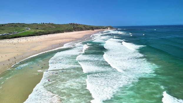 Breathtaking aerial shot showcasing a beautiful beach, gentle waves, and surfers enjoying the water.