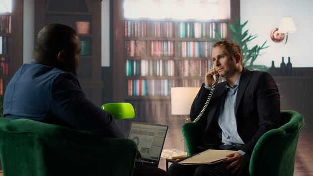 Intelligence officer on a secure line answering phone call in CIA safe house, gathering field information from undercover informants scattered around the city. Sensitive details. Camera A.