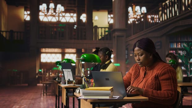 Happy female librarian typing on her laptop in a quiet library workspace, dedicated to organizing resources and mentoring students in their academic journey with pride and expertise. Camera A.