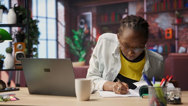 Remote accountant at home checking invoices and entering data on laptop, managing client accounts. Bookkeeper in apartment crosschecking figures between notebook screen and paper files, camera B