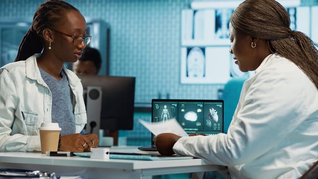 Doctor providing expert advice on health care wellness consulting a patient in a modern facility, evaluating radiology reports and advanced diagnostic tools. Medical therapy. Camera A.