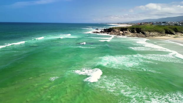 A stunning aerial view highlights the vibrant turquoise waters and rocky shoreline under clear blue skies