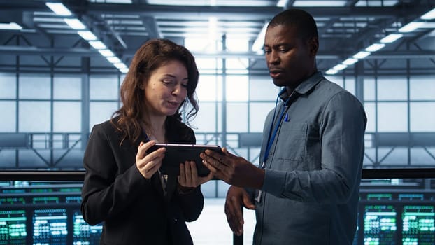 Computer scientists in data center using tablet to develop disaster recovery plans. IT professionals in server farm discussing, testing failover scenarios, protecting data during disruptions, camera B
