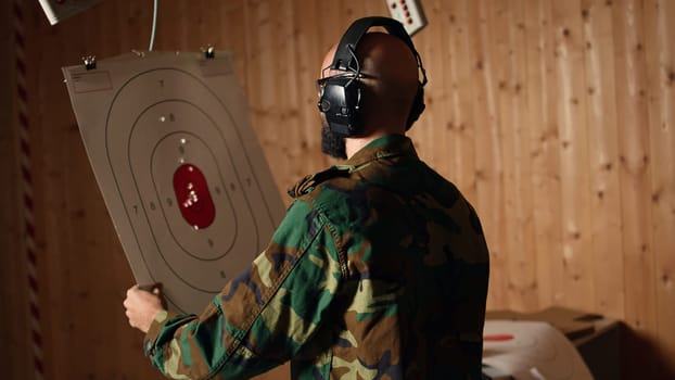 Cheerful army unit in firing range shooting targets with pistol pleased after achieving positive result. Excited soldier training with weapon thrilled after accurately hitting bullseye, camera A