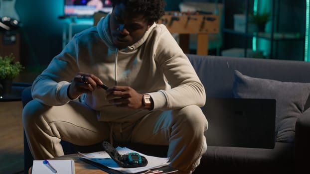 African american diabetic person working from home in his cozy apartment, using an insulin pen and measuring his glucose levels. Young adult with illness uses glucometer. Camera A.