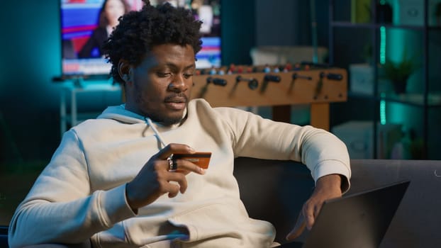Smiling african american man entering card digits to confirm a money transfer, setting up the payment for online shopping on his pc. Happy person feeling good after placing orders. Camera A.